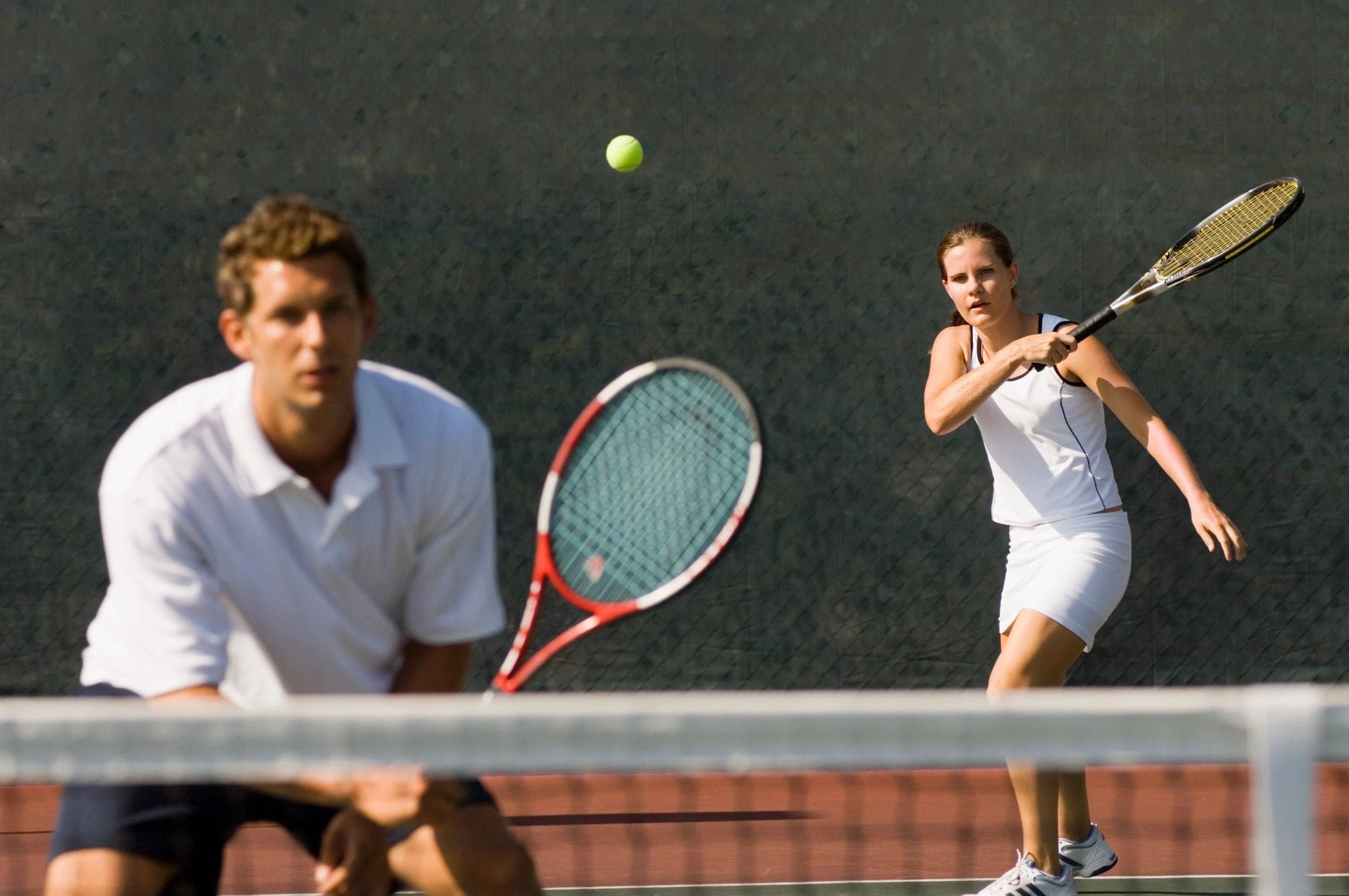 Two men playing tennis on a court with one man swinging at the ball.